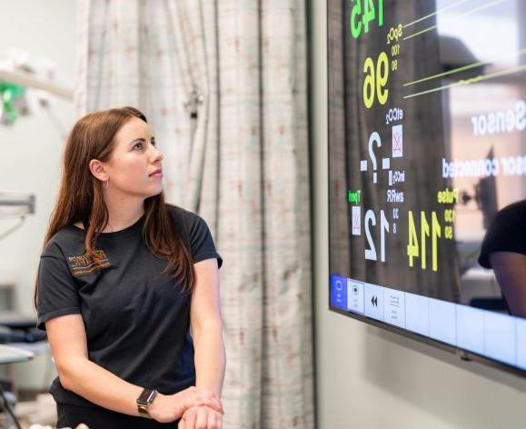 A PA student is shown looking up at a patient monitor. 